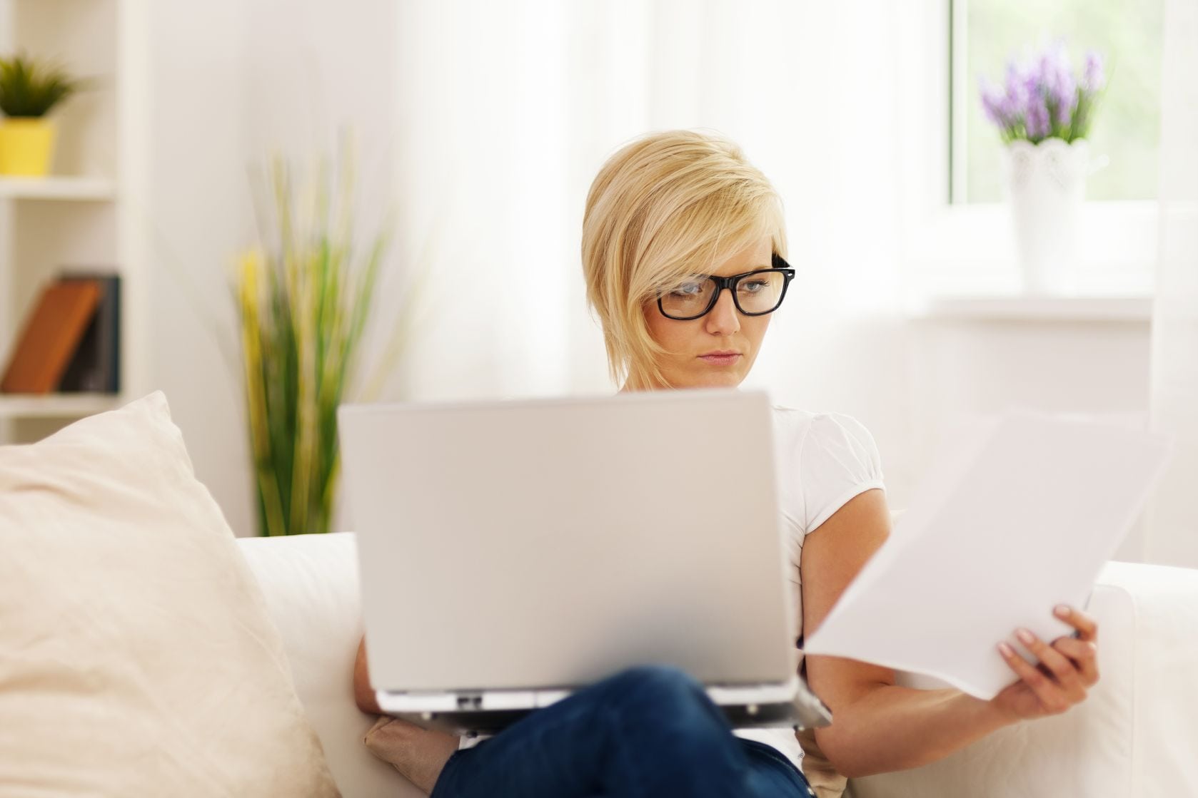 california woman with laptop on lap and reading a paper