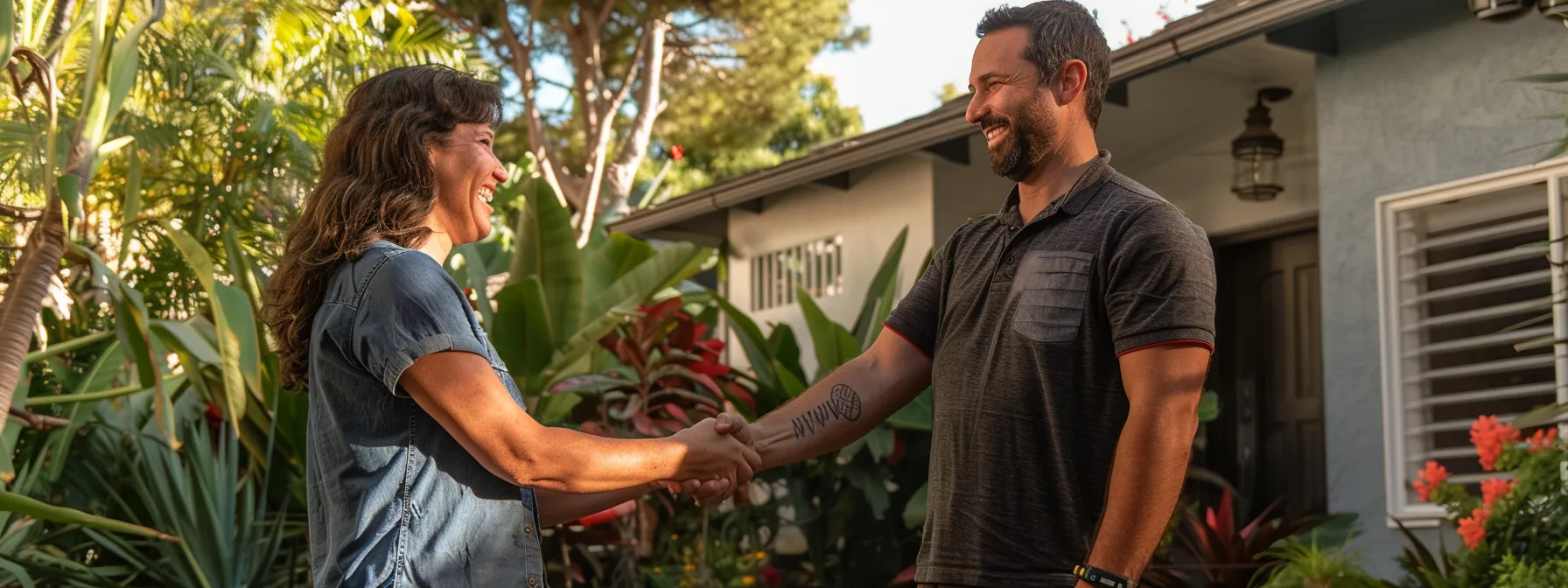 a family smiling as they confidently shake hands with a reputable local moving company in front of their san diego home.