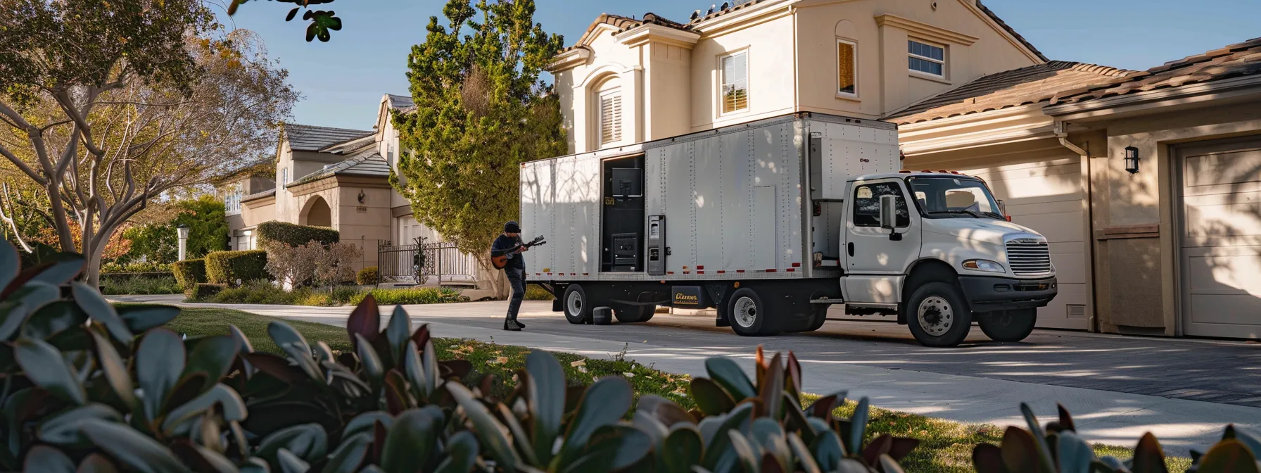 A Moving Truck Parked Outside A House In Irvine, Ca, With A Large Gun Safe Being Carefully Loaded By Movers, Showcasing A Licensed And Insured Moving Company In Action.